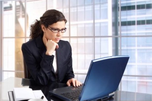 Young female office worker sits in front of her computer screen. Daylight, indoor, office. Dark cloth.