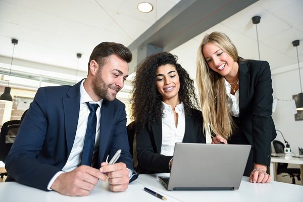 Multi-ethnic group of three businesspeople meeting in a modern office. Two women and a man wearing suit looking at a laptop computer.