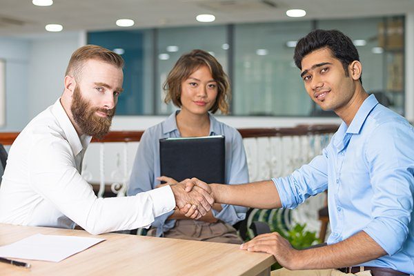 Content Indian candidate shaking hands with company leader at and of job interview. Asian HR manager posing in background. Job interview concept